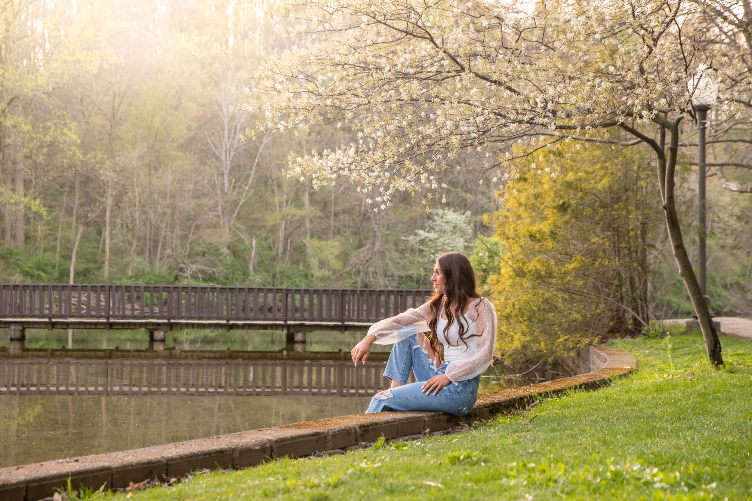 Young woman sitting peacefully by a pond near a wooden bridge in spring park.