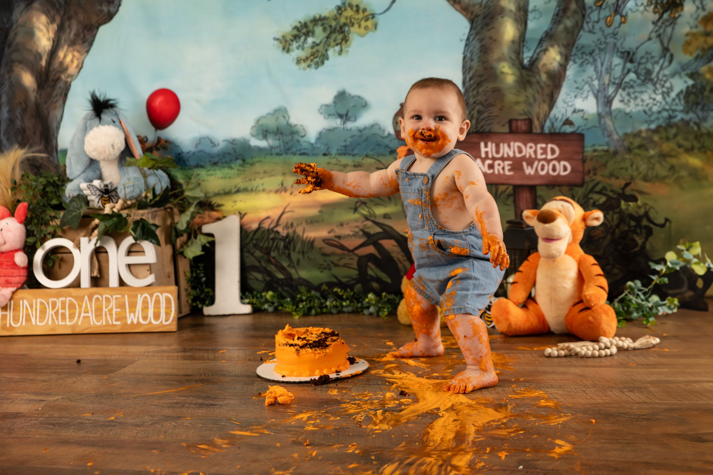 Baby boy covered in cake celebrating first birthday with Winnie the Pooh themed backdrop.