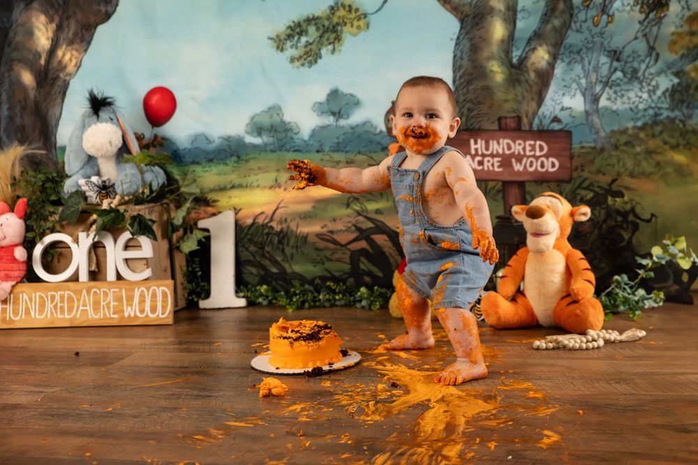 Baby boy covered in cake celebrating first birthday with Winnie the Pooh themed backdrop.