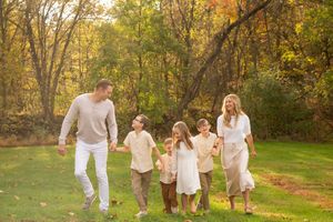 A happy family of six walks together in an autumn park with golden trees.