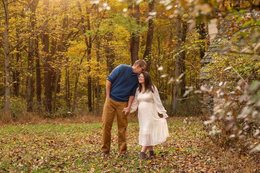 A couple holds hands and smiles in a colorful autumn forest setting.