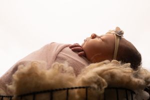 Sleeping newborn baby wrapped in pink swaddle wearing delicate floral headband.