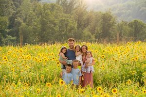 A joyful family of seven poses in a vibrant sunflower field at sunset.