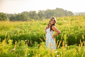 Teenage girl in blue floral dress posing in a sunlit wildflower meadow at golden hour.