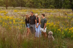 Family of four with a fluffy dog standing in a wildflower meadow during golden hour in fall.
