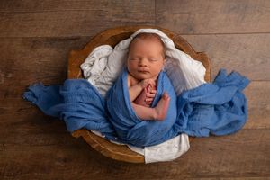 A newborn baby wrapped in blue cloth sleeps peacefully in a wooden bowl.