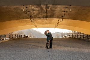 Couple sharing a kiss under an arched golden bridge in a dramatic urban outdoor setting.