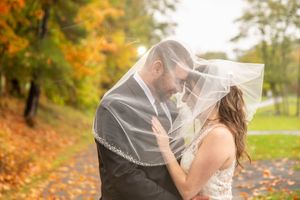 Bride and groom sharing a romantic moment under a veil surrounded by colorful autumn foliage.