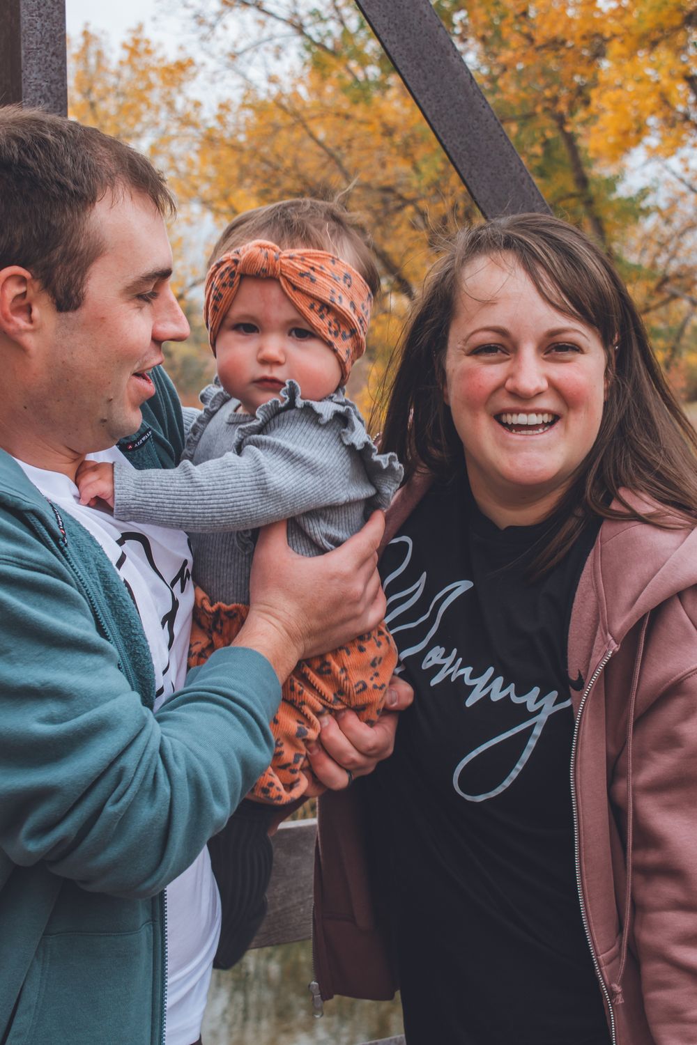 Happy family with a smiling mother wearing a Mommy shirt holding their baby girl in autumn park.