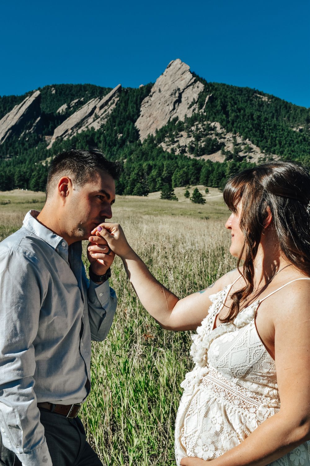 Couple sharing a romantic moment in a field with the Flatirons mountains in Boulder, Colorado behind them.