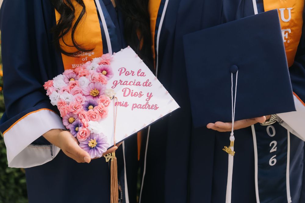 Graduation caps decorated with flowers and Spanish text at a university commencement ceremony.