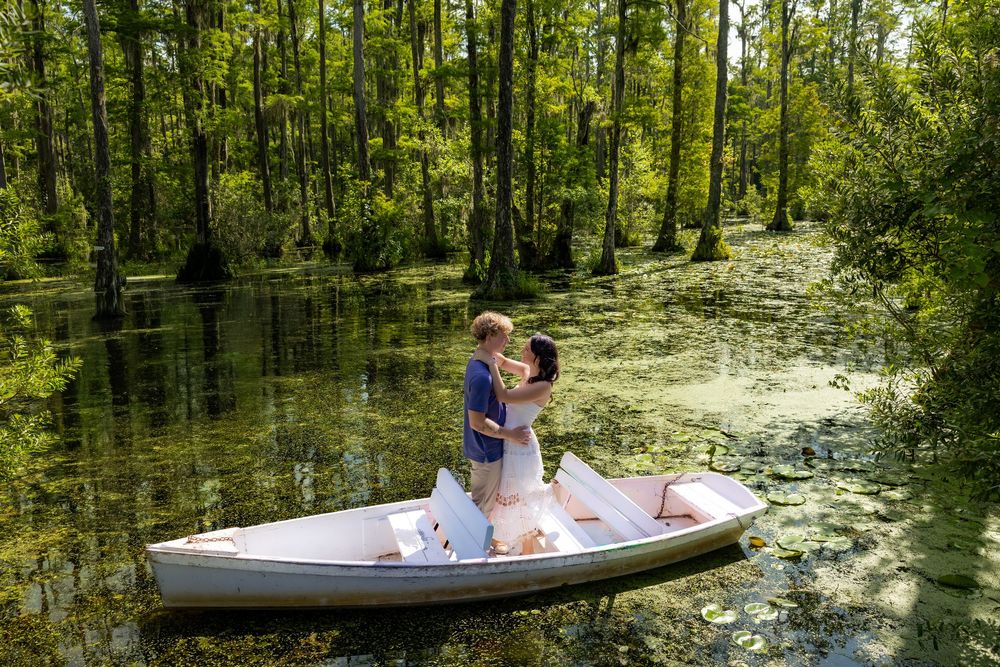 Couple embracing in a white rowboat surrounded by lush green swamp trees and algae-covered water.