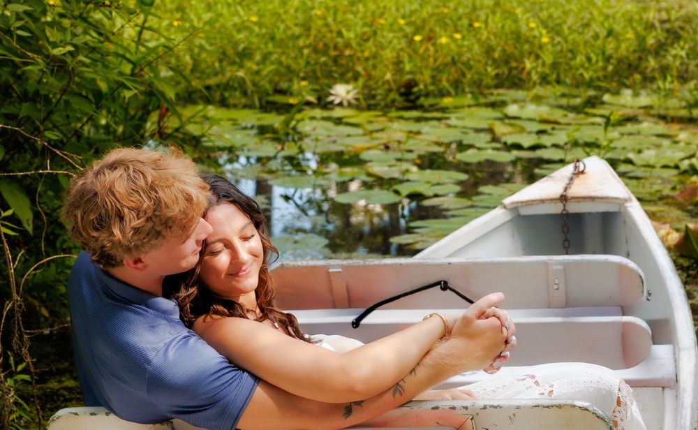 Romantic couple embracing in a white rowboat surrounded by lily pads on a serene pond.