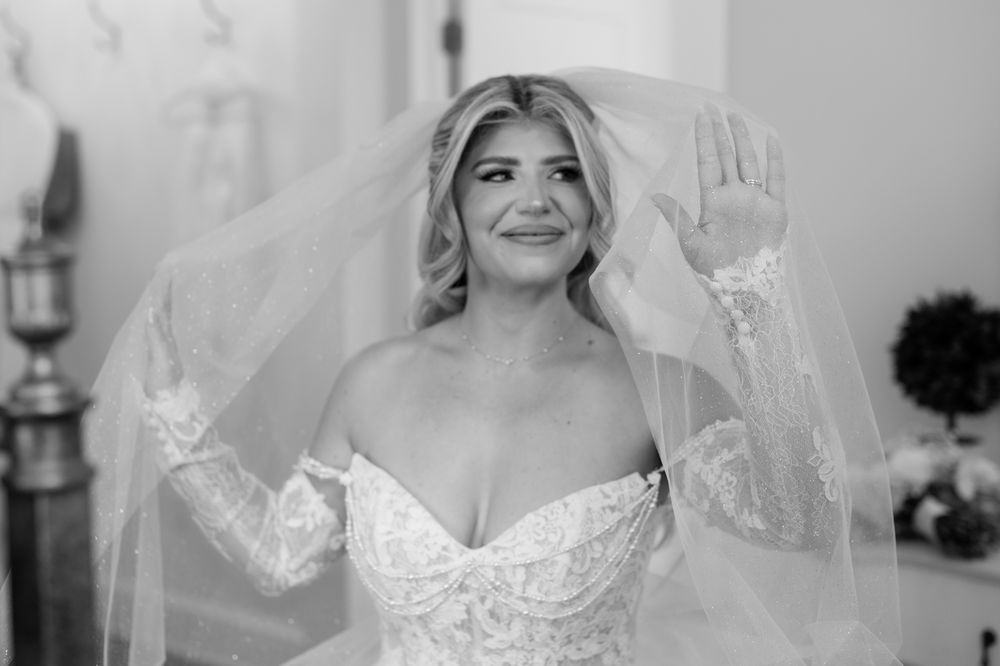 Bride in strapless lace wedding dress lifting veil and smiling in black and white photo.
