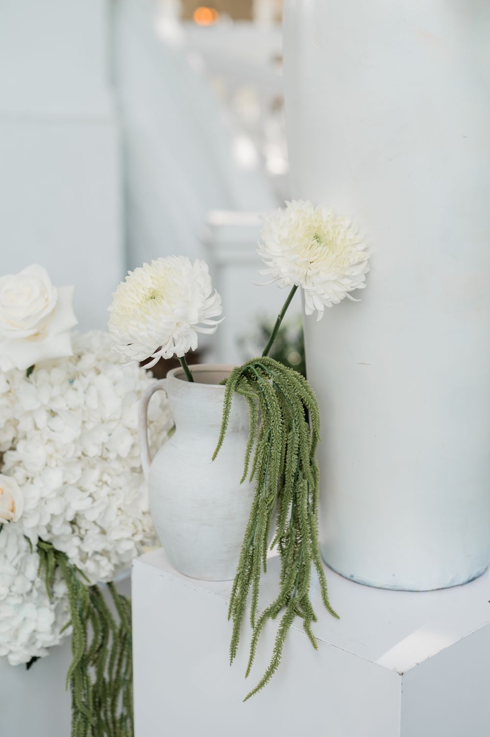 Elegant white wedding decor with hydrangeas, dahlias, and hanging amaranthus in ceramic vases.