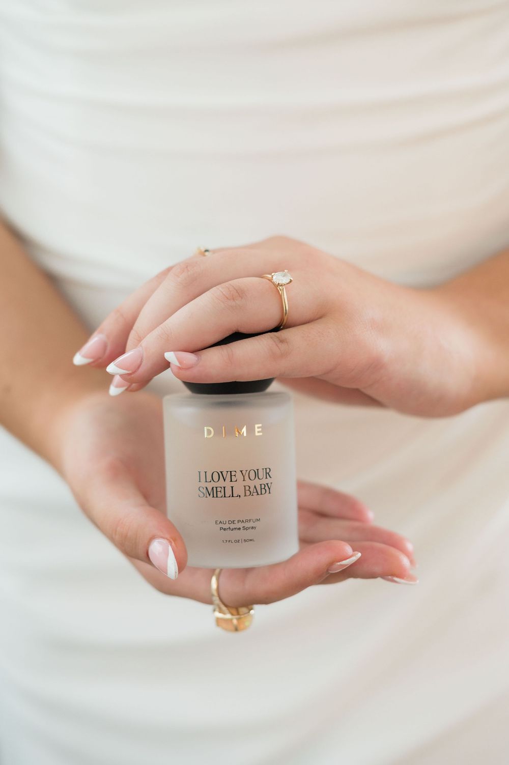 Bride holds DIME perfume spray bottle showcasing diamond engagement ring and French manicure.