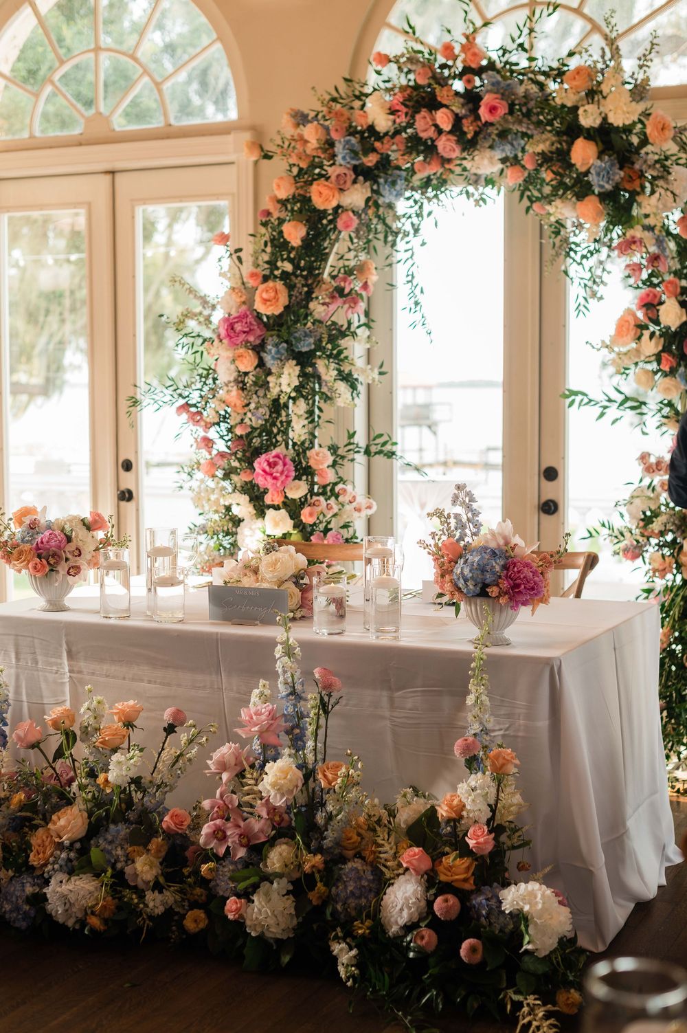 Elegant wedding reception table adorned with a stunning floral arch and colorful blooms in peach, pink, and blue.