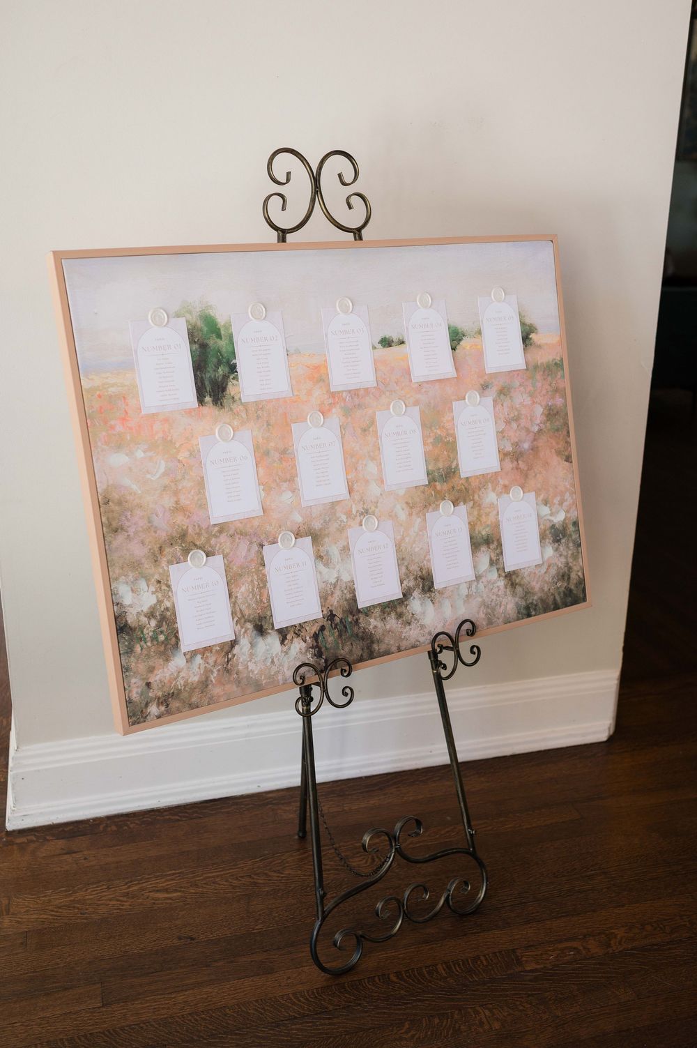 Elegant wedding seating chart displayed on a decorative iron easel, featuring white name cards on a floral canvas backdrop.