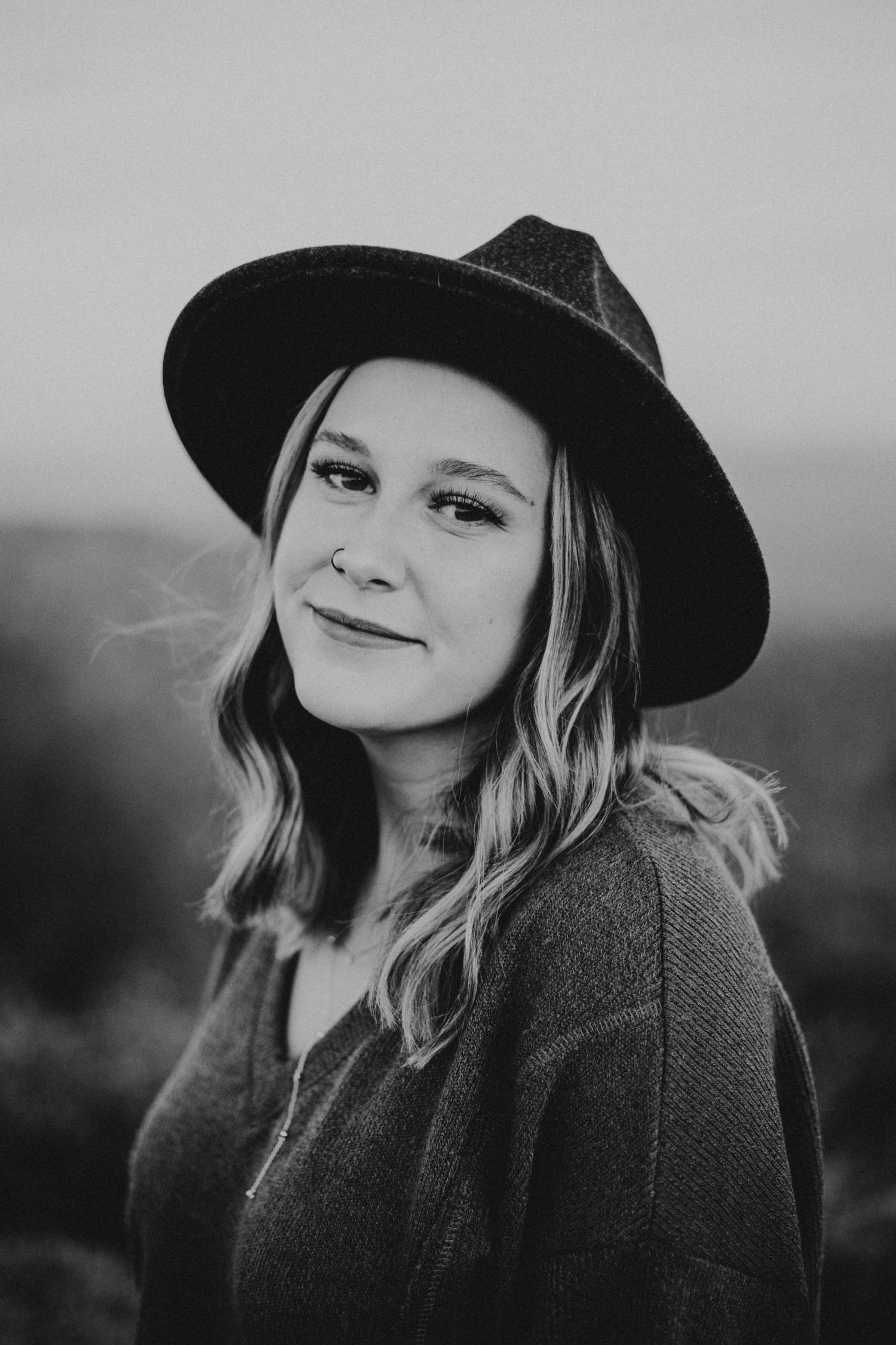 Portrait of person wearing black hat against blurred natural background in black and white.