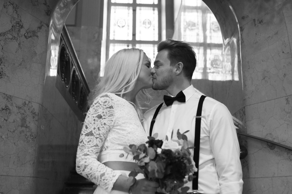 Black and white romantic wedding portrait under arched window with lace dress and bouquet.
