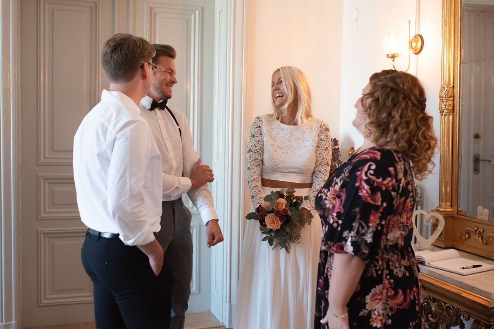 Small wedding gathering with bride in lace dress talking to guests in classic interior.