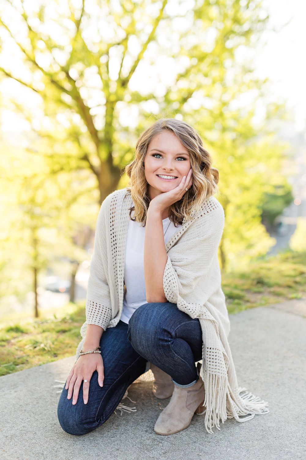 A person wearing a knit cardigan and jeans poses on a pathway during golden hour.