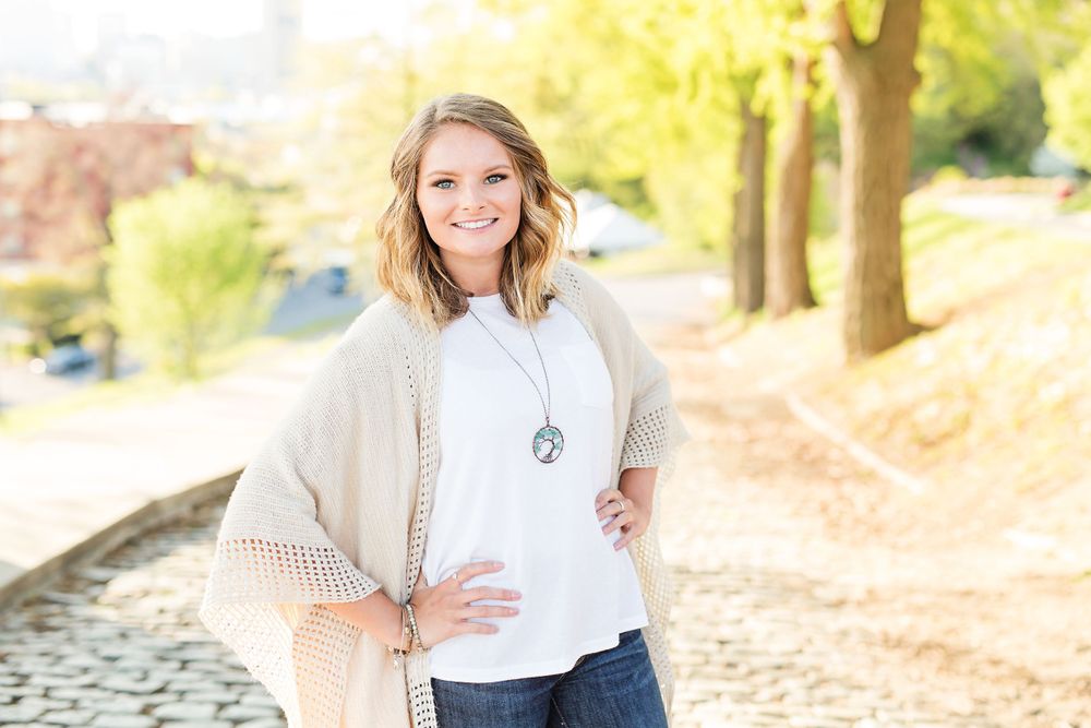A person in a flowing cream cardigan and pendant necklace poses on a sunny path.
