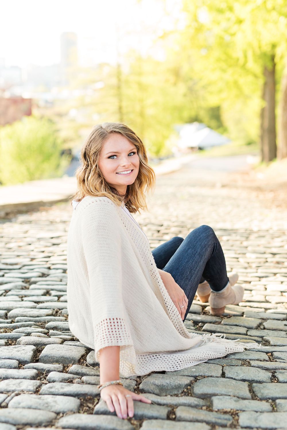 A person in casual attire sits on cobblestone steps during a sunny autumn day.