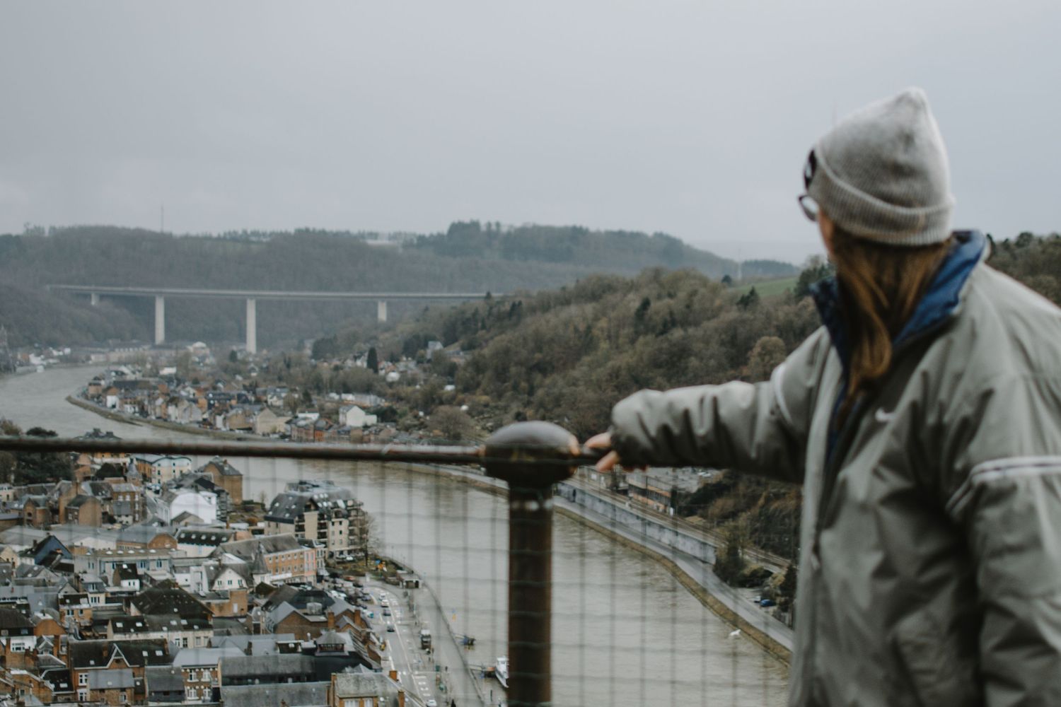 Person in winter coat overlooking cityscape from observation deck.