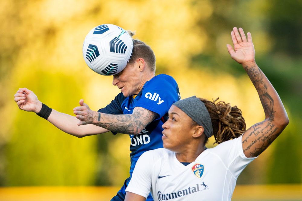 A soccer player heads the ball over her defender.