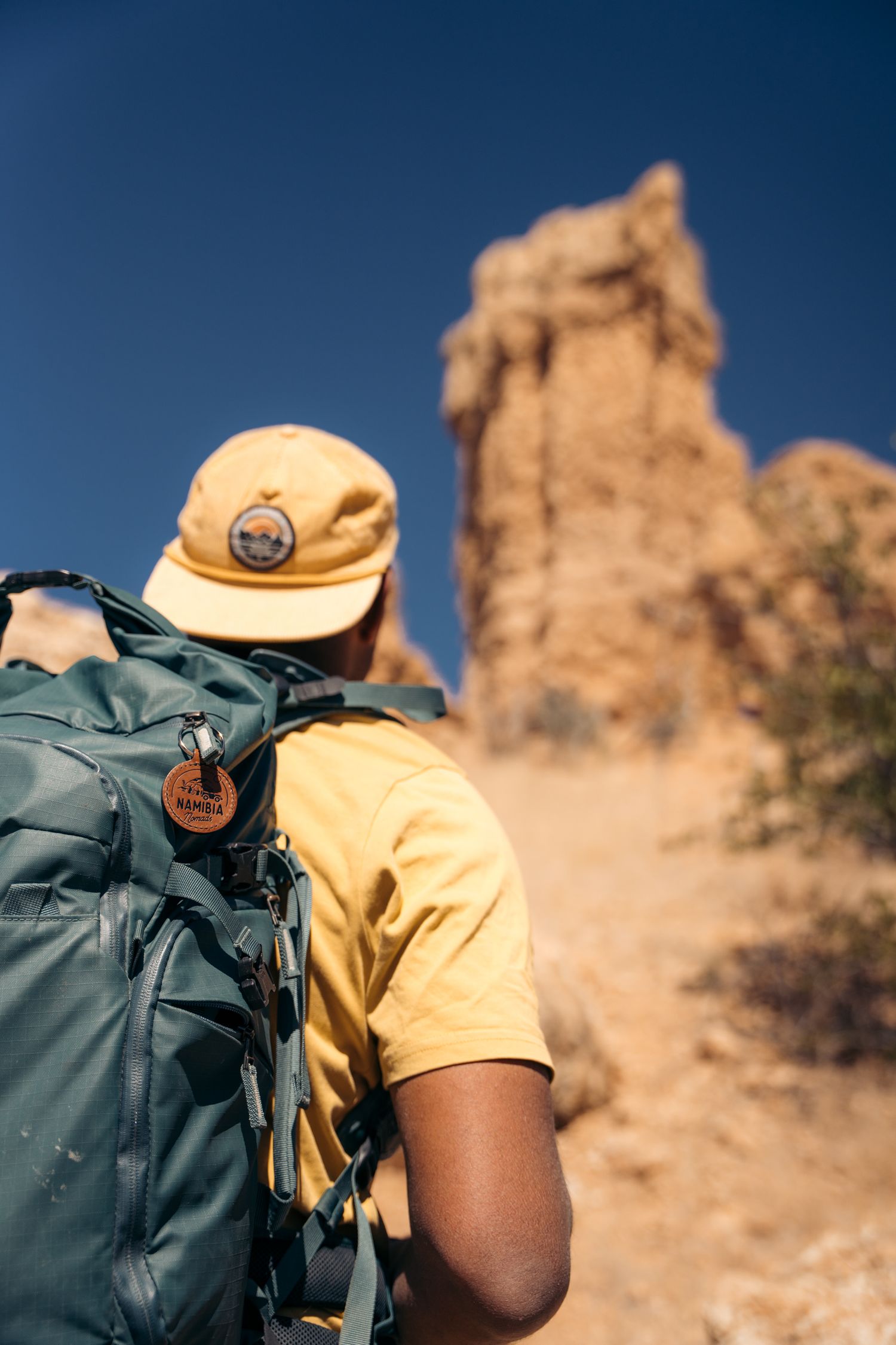 homme de dos avec son sac à dos qui marche vers vingerklip, une formation rocheuse unique en namibie