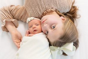 An intimate overhead portrait of a sleeping newborn and sibling lying together on beige fabric.