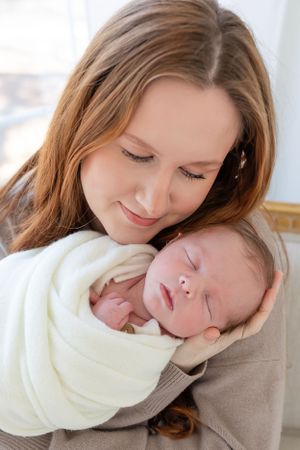 An intimate portrait showing a gentle embrace of a sleeping newborn wrapped in white.