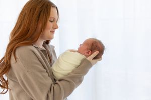 A gentle moment captured as a parent in beige holds a swaddled newborn against a white background.