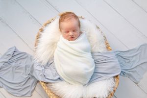 Sleeping newborn swaddled in white blanket resting in basket with fur lining and blue fabric.
