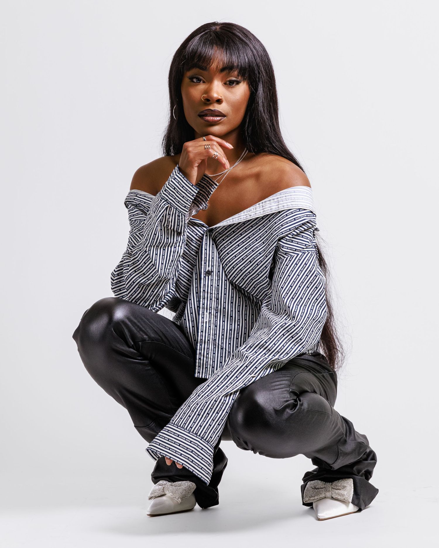Fashion model poses in off-shoulder striped shirt and black pants against white background.