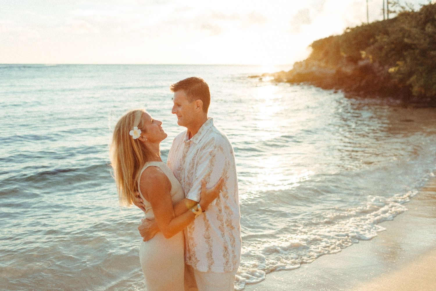 couple holds eachother, with their feet in the water during a hawaiian sunset