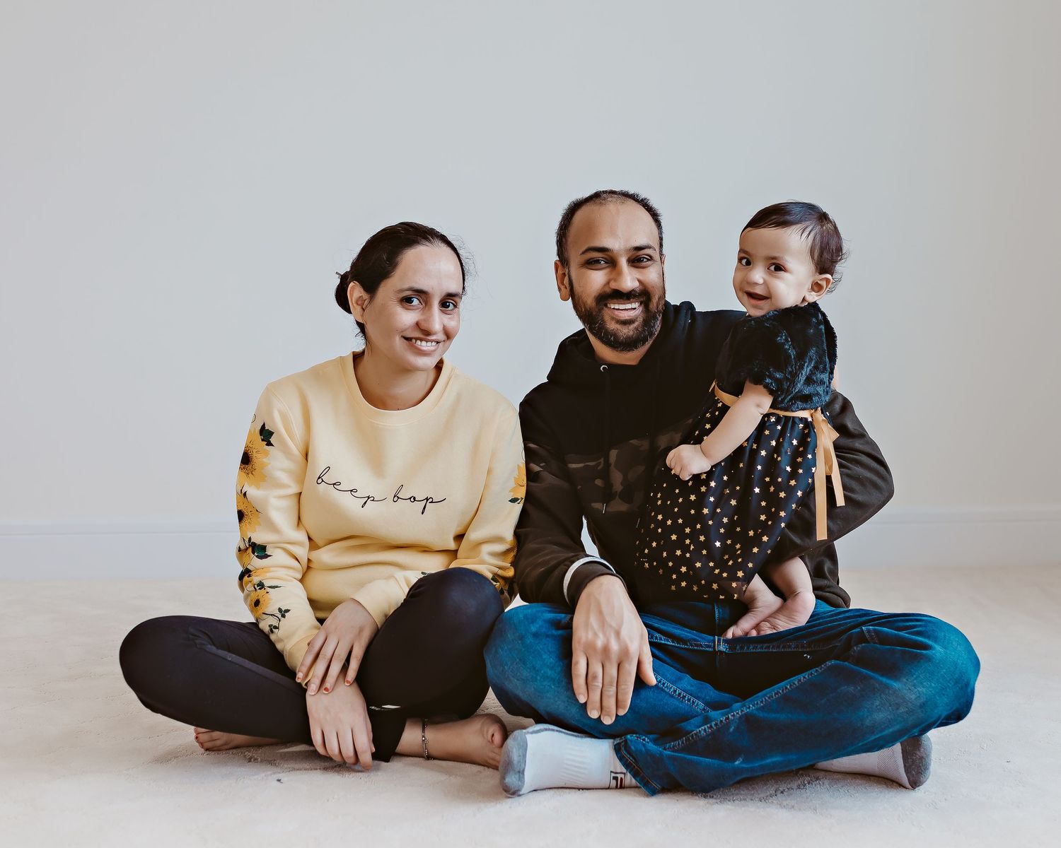 Family sitting together on floor against white wall in casual attire.