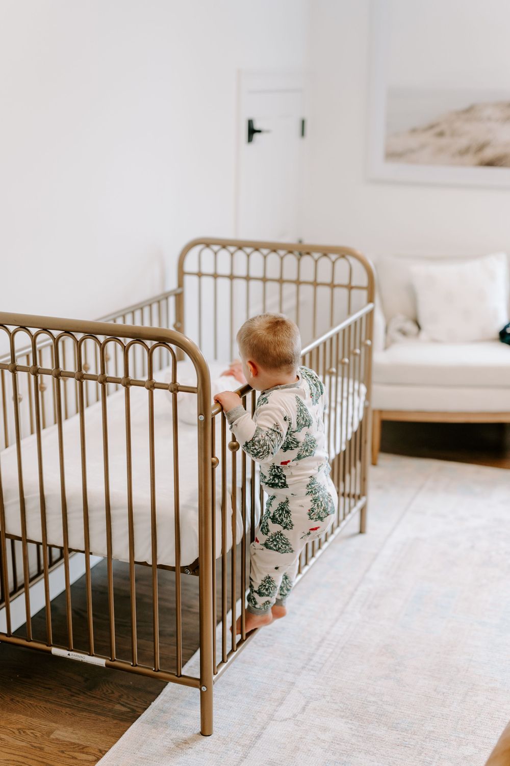 Vintage-style brass baby crib with floral bedding in bright white nursery.