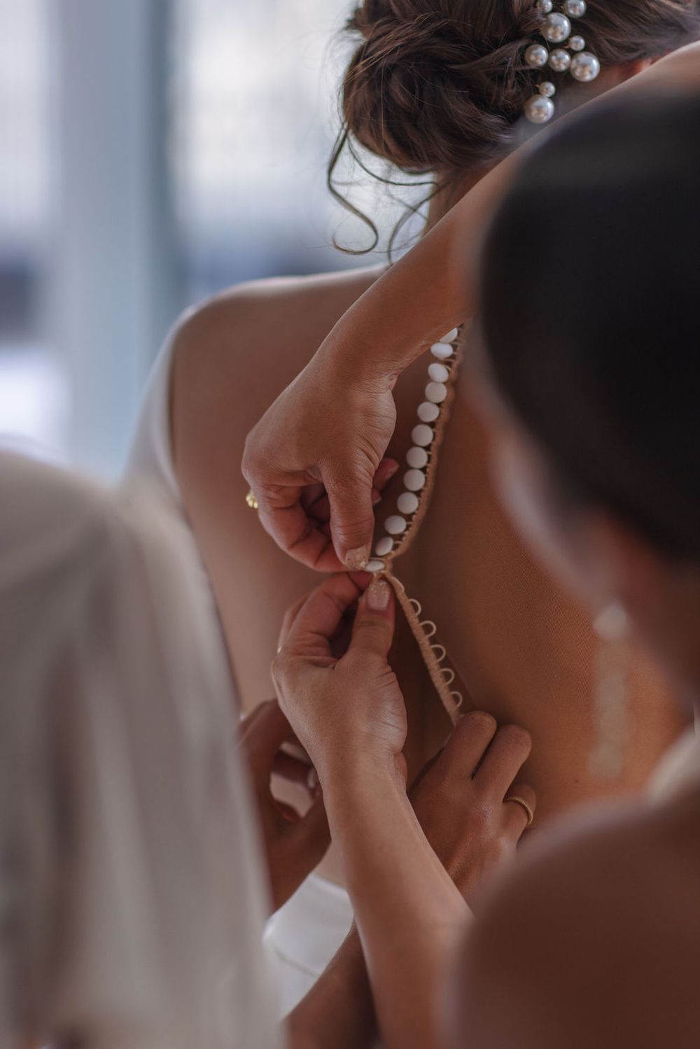 Close-up detail of pearl buttons being fastened on back of wedding dress.