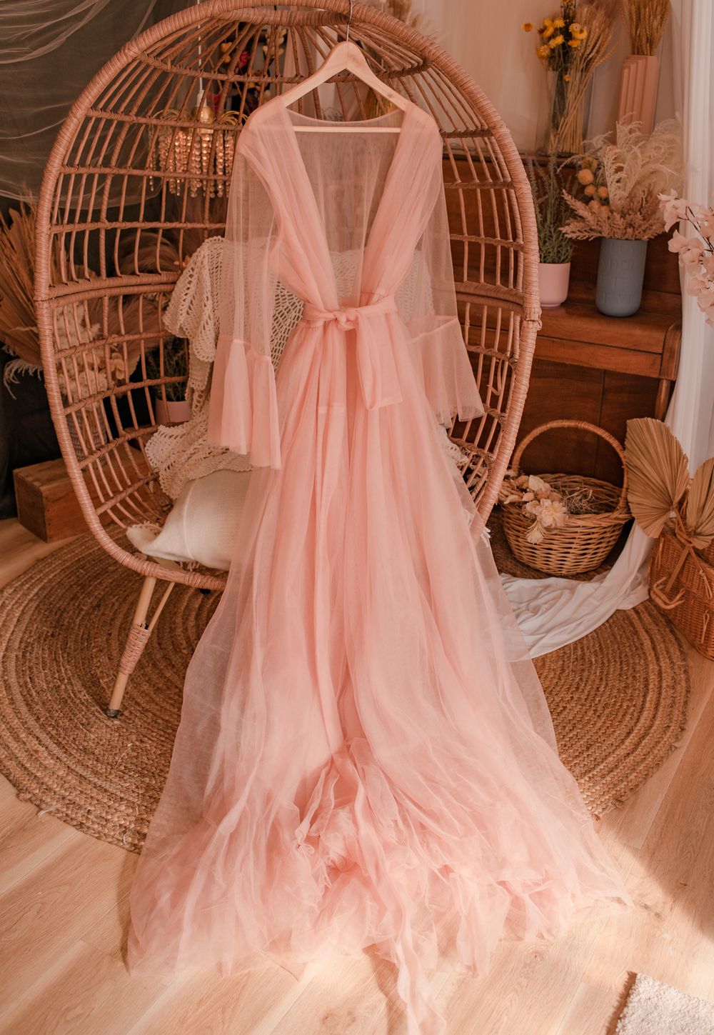 Ethereal blush pink tulle gown with flowing sleeves displayed on rattan peacock chair.