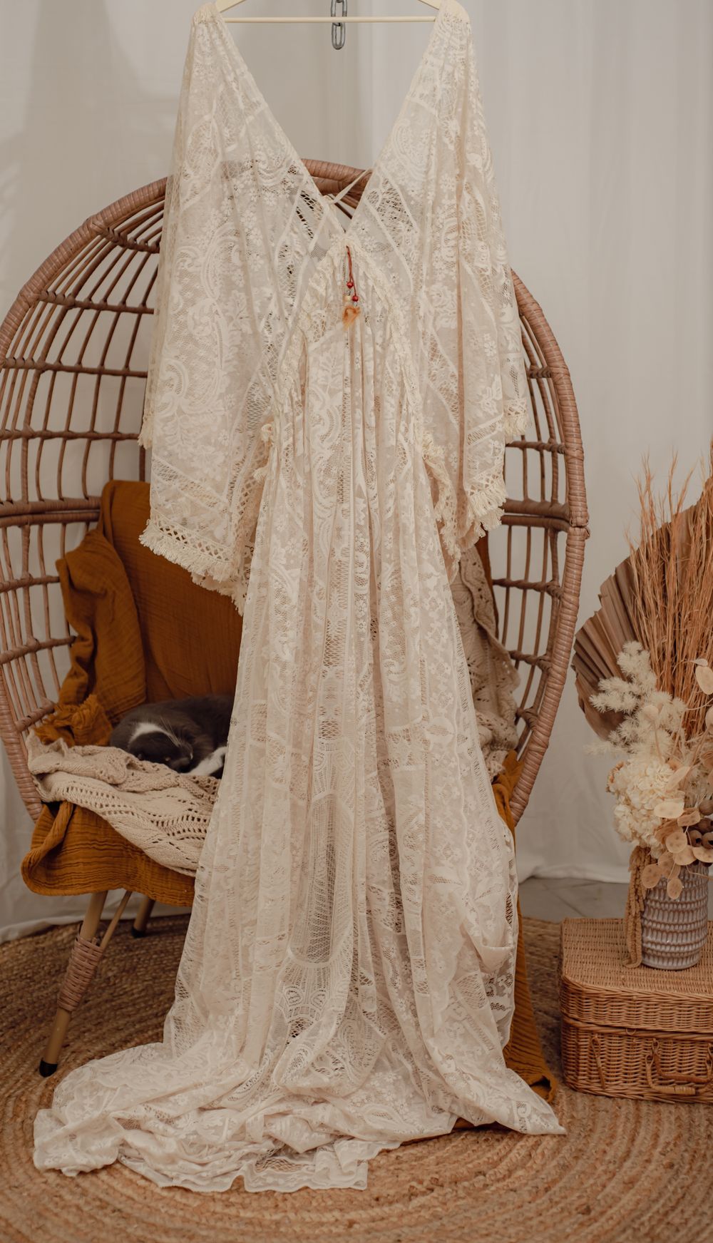 A romantic lace wedding dress with flowing sleeves displayed on a rattan chair.