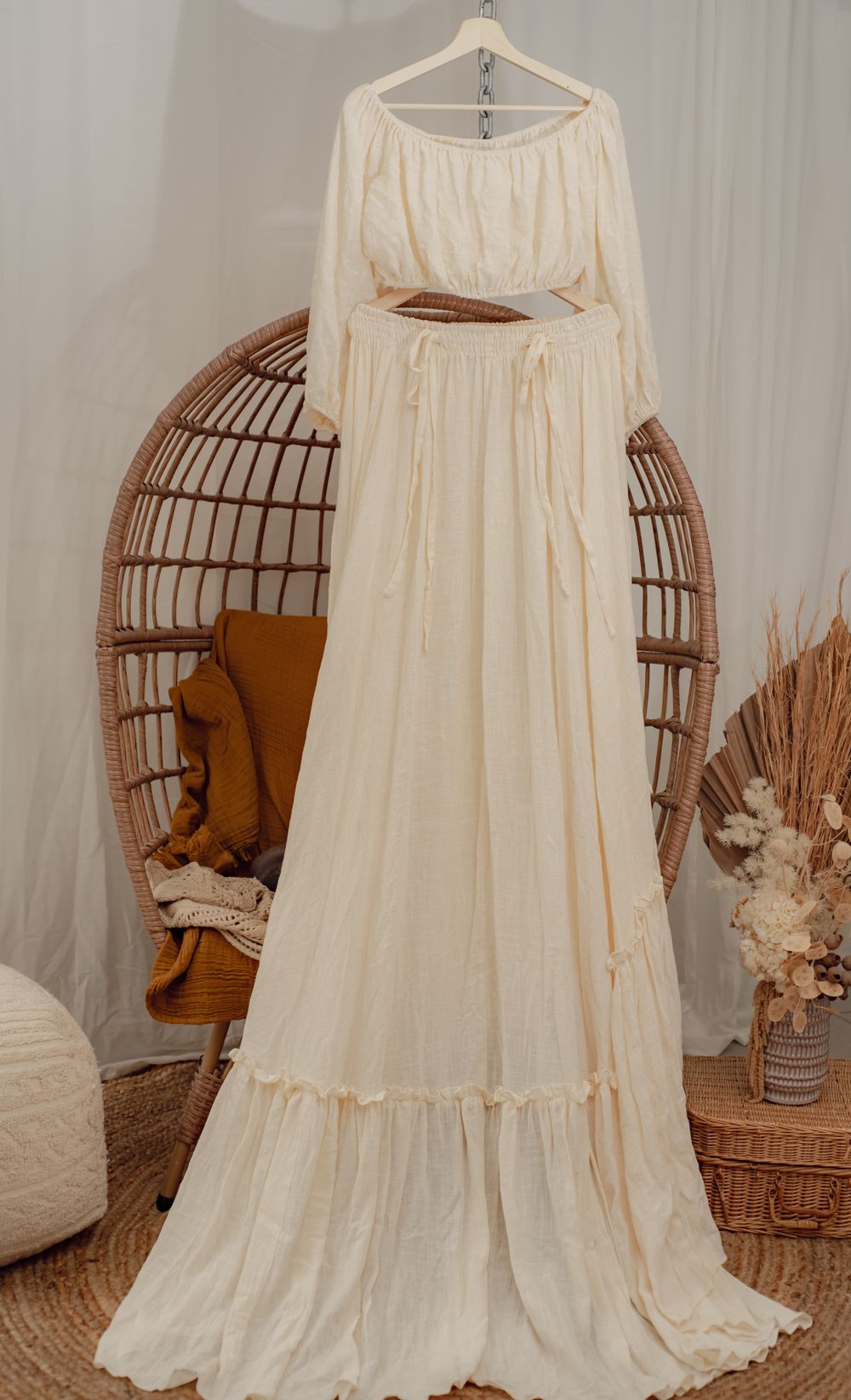 An ethereal cream colored maxi dress with long sleeves displayed against a rattan chair.