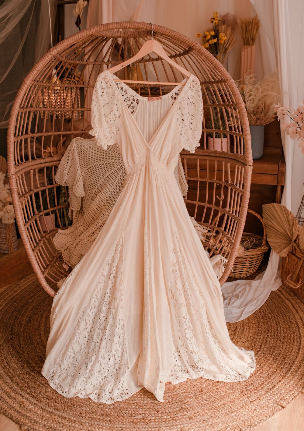 Romantic white lace maxi dress with flutter sleeves displayed on vintage rattan peacock chair.