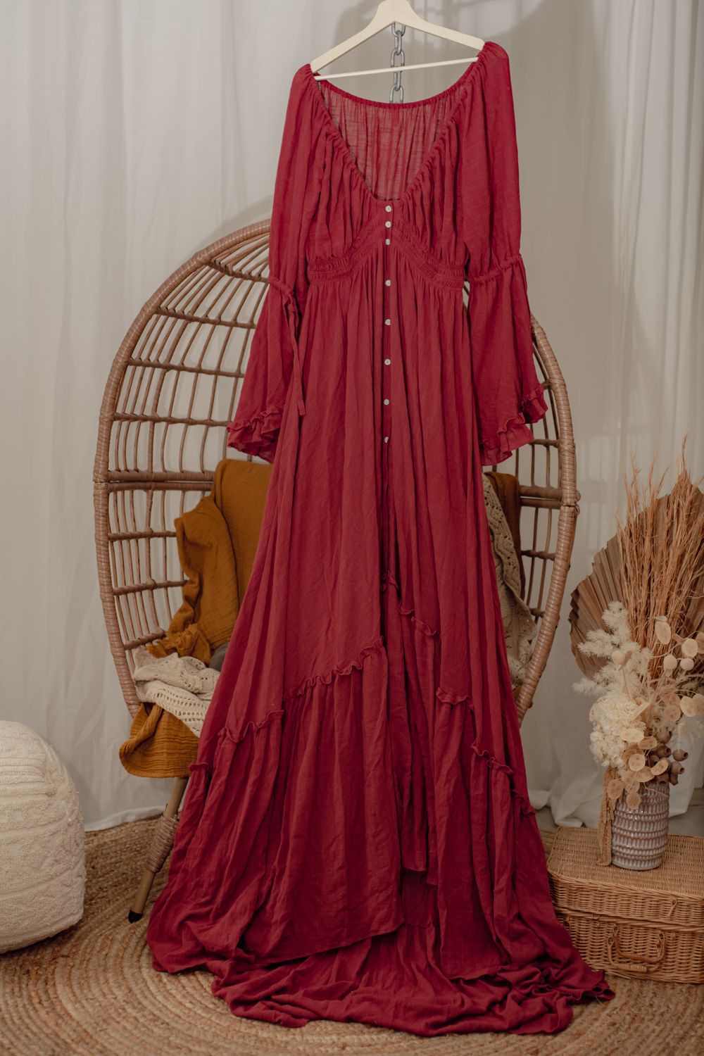 A flowing red maxi dress with button details displayed on a rattan peacock chair.