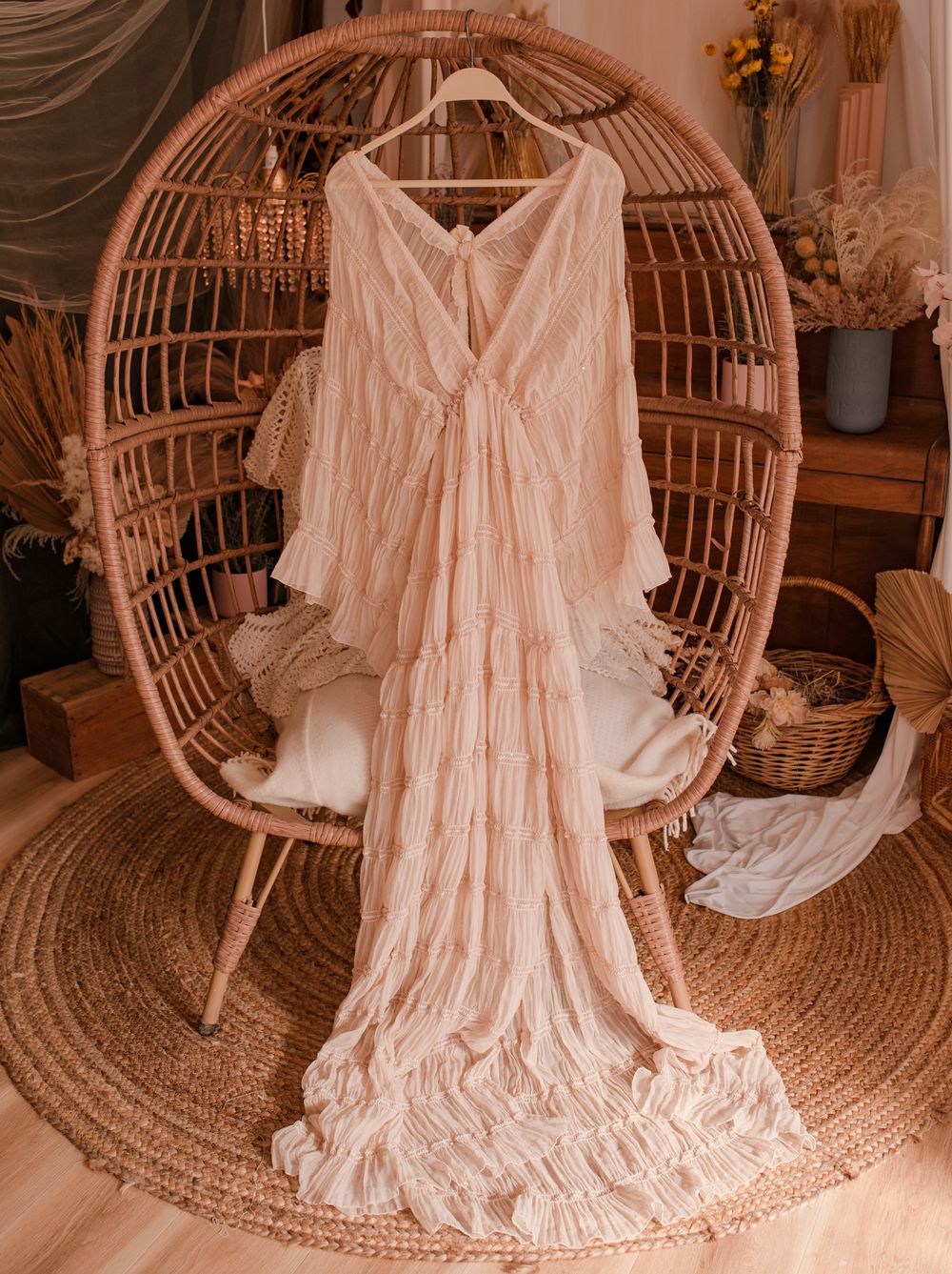 Delicate cream-colored flowy dress with ruched details displayed on rattan peacock chair.