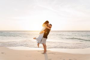 Couple embracing on a sandy beach at sunset with golden light and ocean waves in the background.