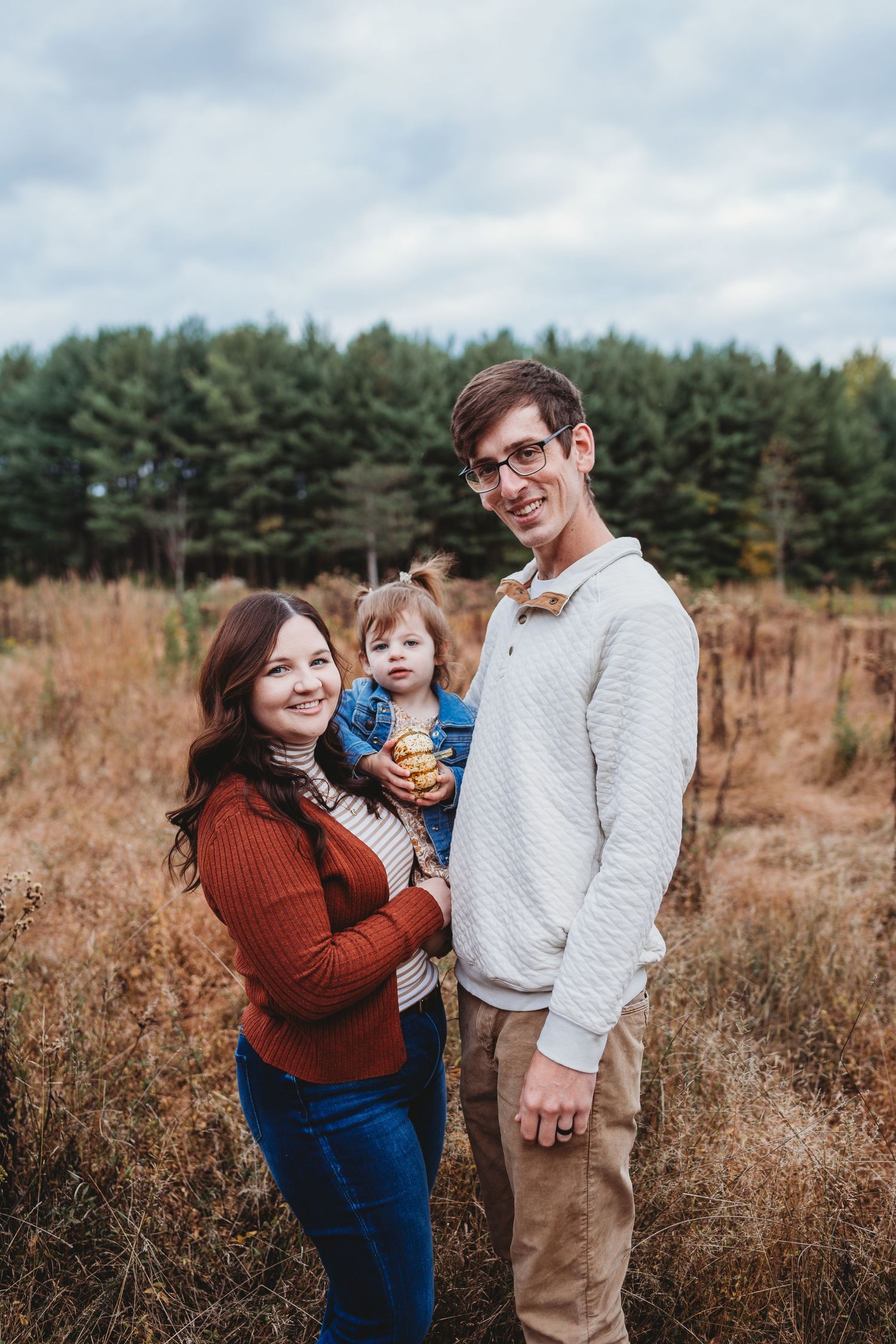 Happy family poses together in autumn field surrounded by pine trees.