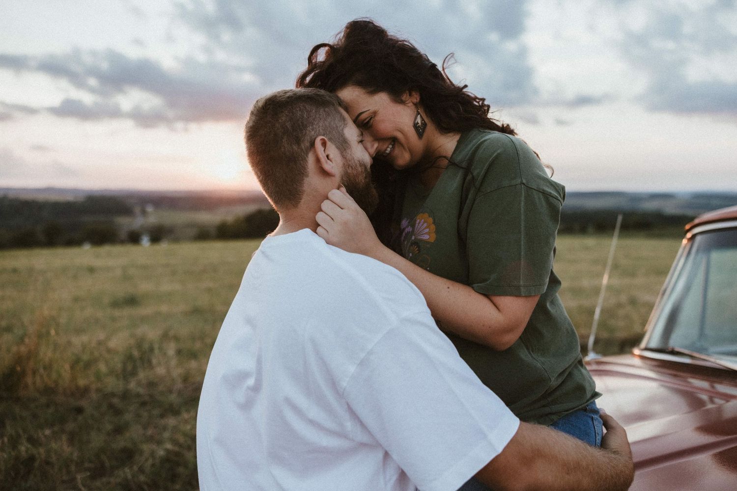 woman sitting on top of a red ford f100 truck smiling down at boyfriend