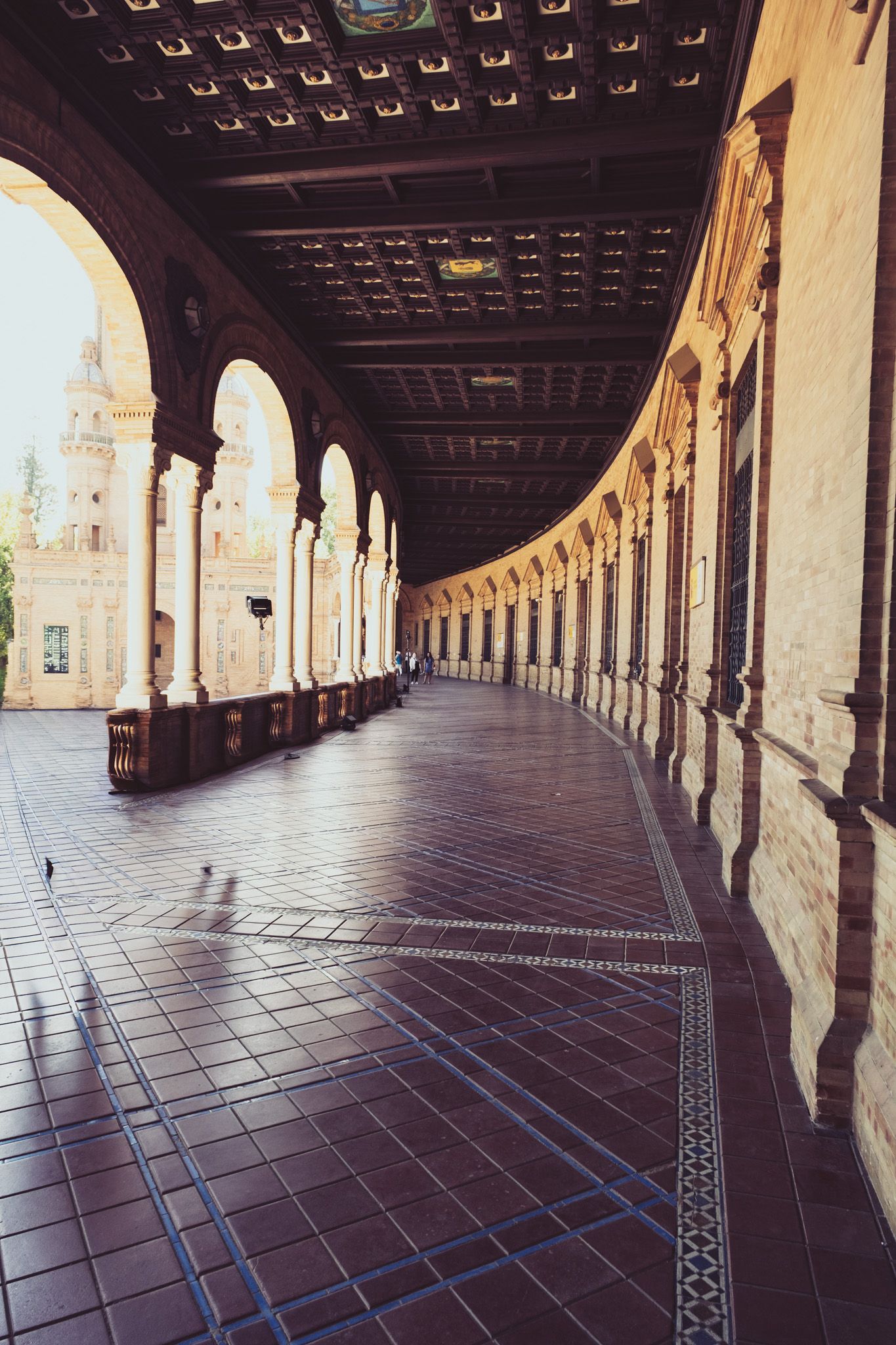 Long arched corridor with ornate wooden ceiling and tiled floor at Plaza de Espana Seville Spain.